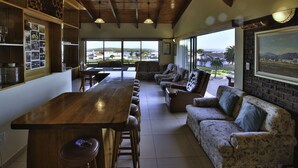 A spacious living area with a wooden bar, comfortable seating, and large windows offering a view of the outdoors. - Dasklip Langebaan 8-sleeper (Langebaan)