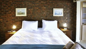 A hotel room with a brick wall, a large bed with white linens, two bedside tables with lamps, and two framed pictures on the wall. - Dasklip Langebaan 8-sleeper (Langebaan)