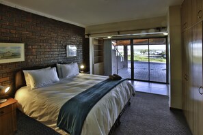 A bedroom with a large bed, a brick wall, a nightstand, a lamp, and a view through a sliding door to an outdoor area. - Dasklip Langebaan 8-sleeper (Langebaan)