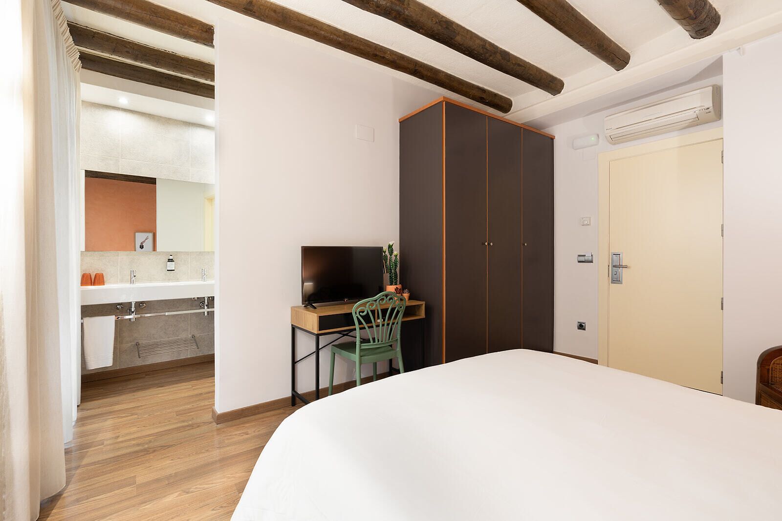 Un dormitorio con cama, escritorio y silla, armario, y un baño visible a través de una puerta abierta.