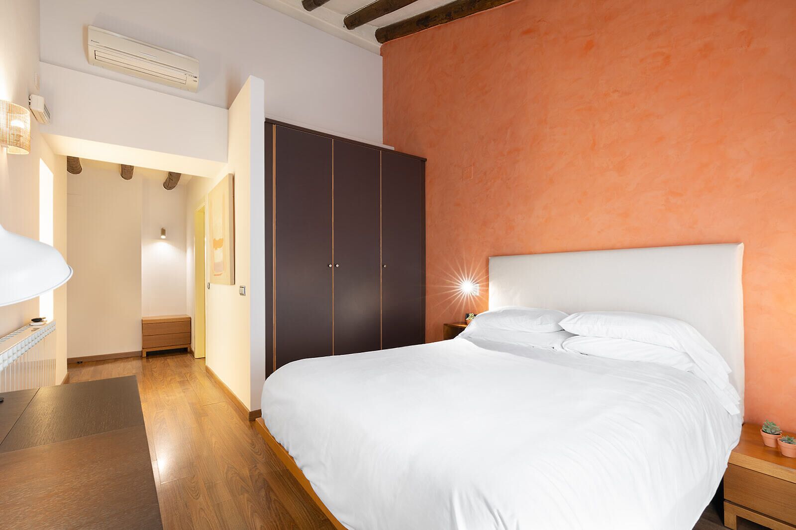A bedroom with a bed, a wardrobe, a bedside table, and a lamp.