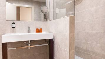 A modern bathroom with a glass shower enclosure, a white sink with a mirror above it, and a dark brown vanity.