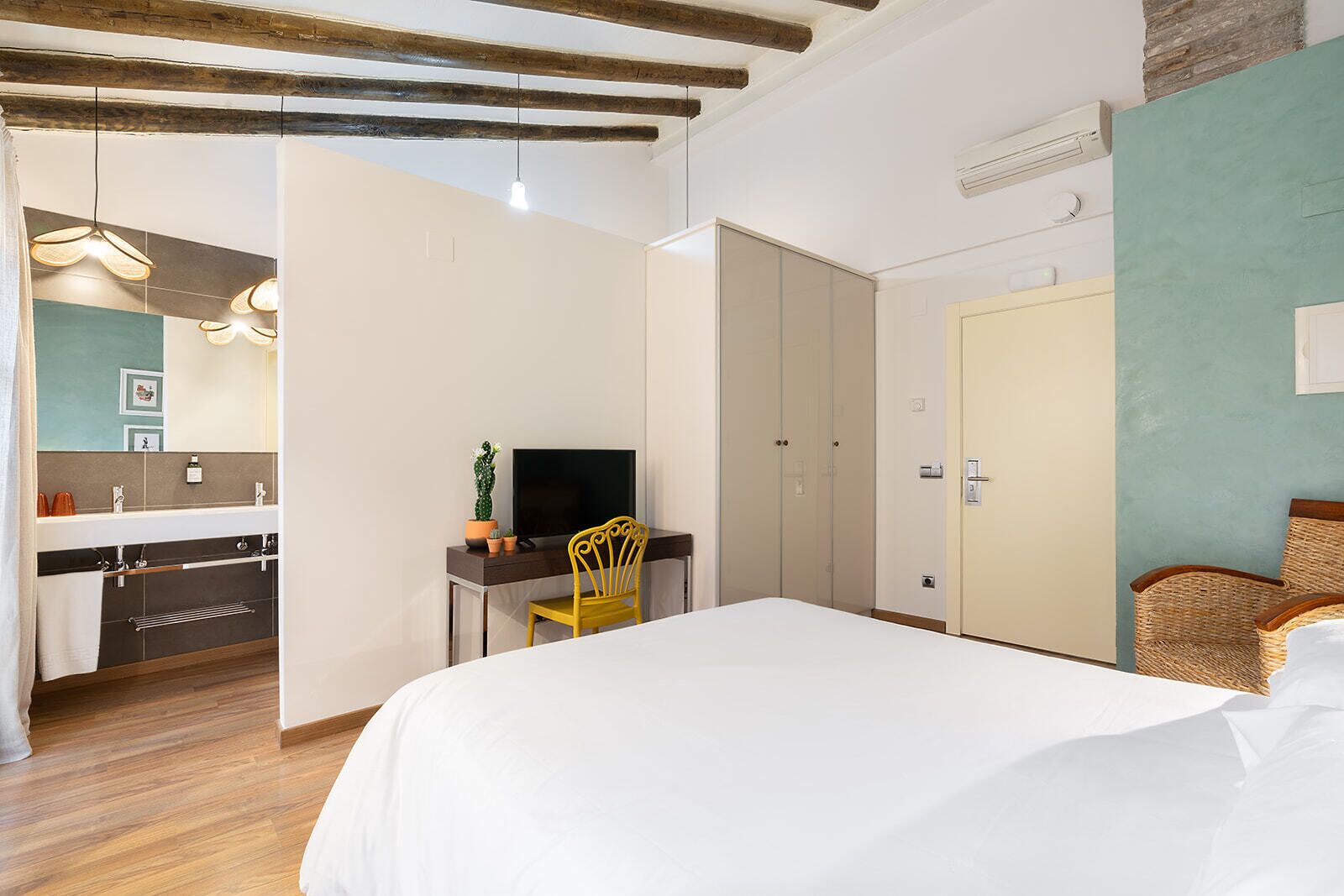 Un dormitorio con cama, escritorio y silla, televisor, armario y baño con lavabo y espejo.
