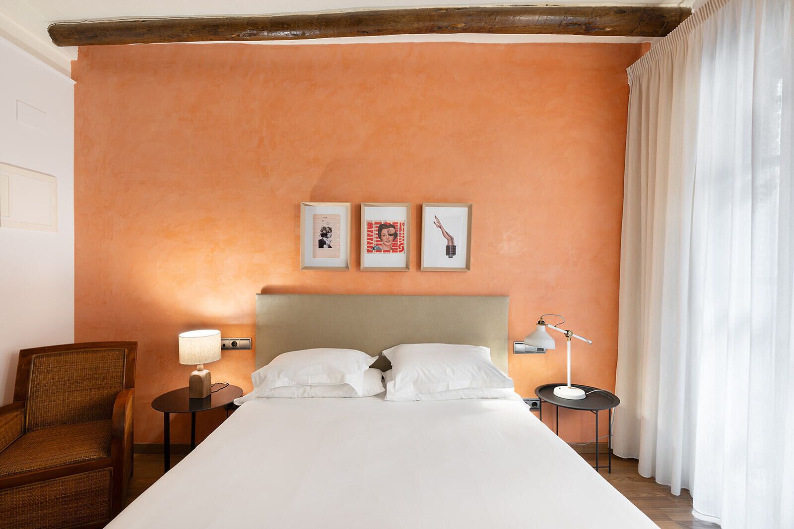 A hotel room with a large bed, two bedside tables, a chair, and a wall with three framed pictures.