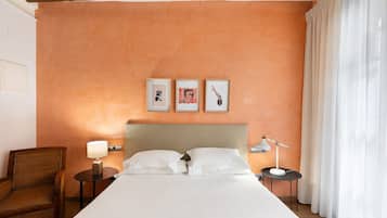 A hotel room with a large bed, two bedside tables, a chair, and a wall with three framed pictures.
