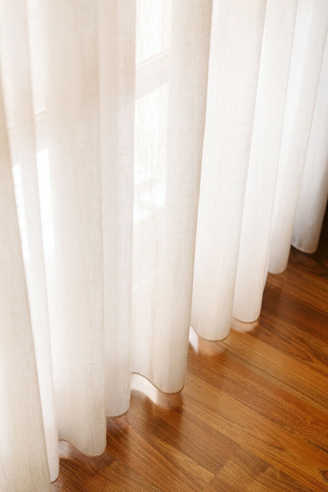 A close-up of white curtains hanging on a wooden floor.