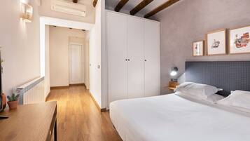 A bedroom with a large bed, a nightstand, a wall-mounted lamp, and a framed picture.