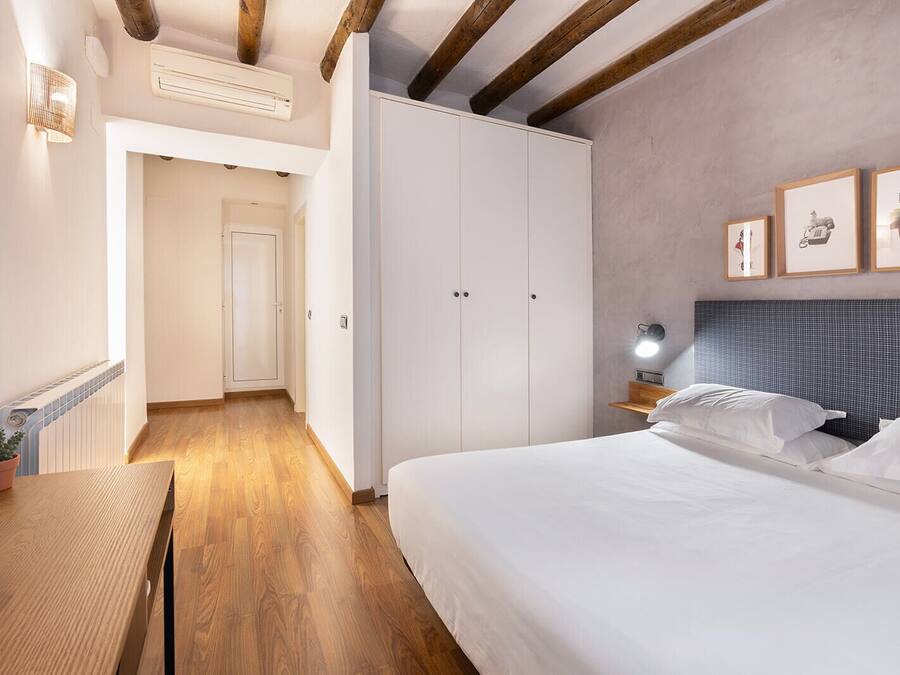 A bedroom with a large bed, a nightstand, a wall-mounted lamp, and a framed picture.