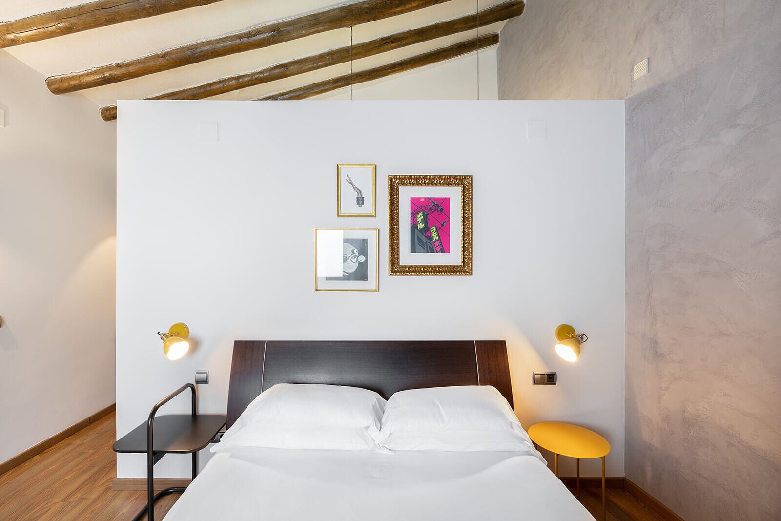 A hotel room with a bed, two wall-mounted lamps, and three framed pictures on the wall.