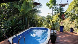 A swimming pool with a wooden deck, surrounded by lush greenery and hanging planters. - Magic Mena Rainforest Retreat by Tiny Away (Mena Creek)