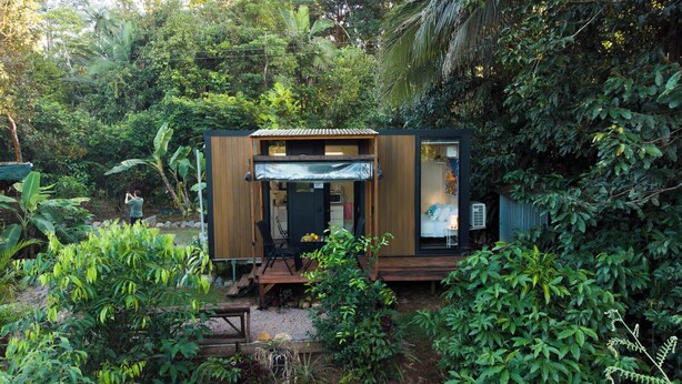 A small, modern cabin with a wooden exterior, a covered entrance, and a visible kitchen area. - Magic Mena Rainforest Retreat by Tiny Away (Mena Creek)