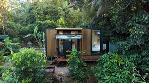 Une petite cabane moderne, avec une façade en bois, une entrée abritée et une cuisine ouverte.