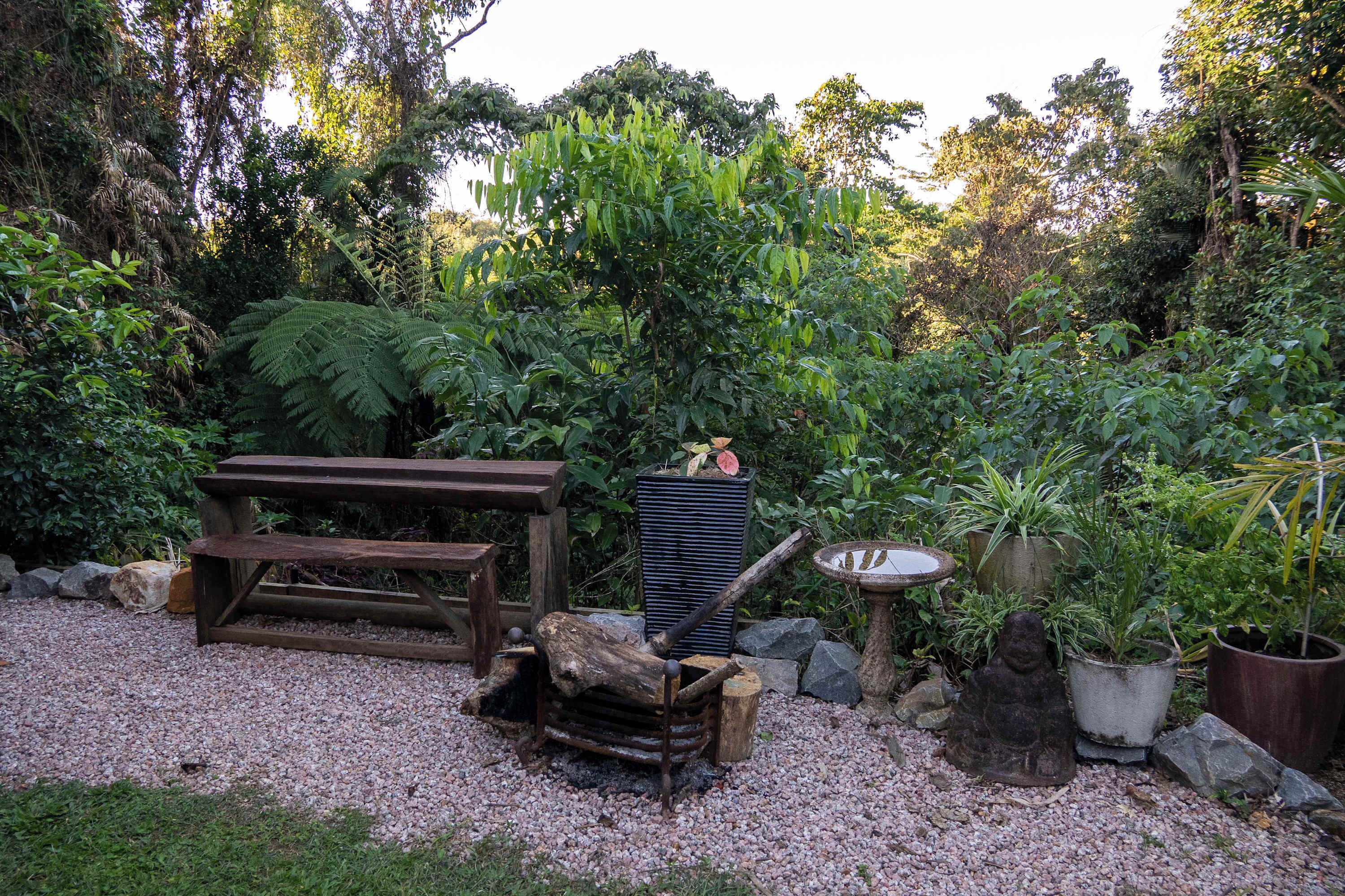 Un jardin avec un banc en bois, un foyer rustique et diverses plantes en pot.