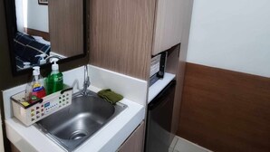 A compact kitchen with a stainless steel sink, a dish drying rack, and a green bottle of dish soap.
