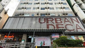 A tall building with multiple floors, a staircase leading to the entrance, and a banner advertising a local event.
