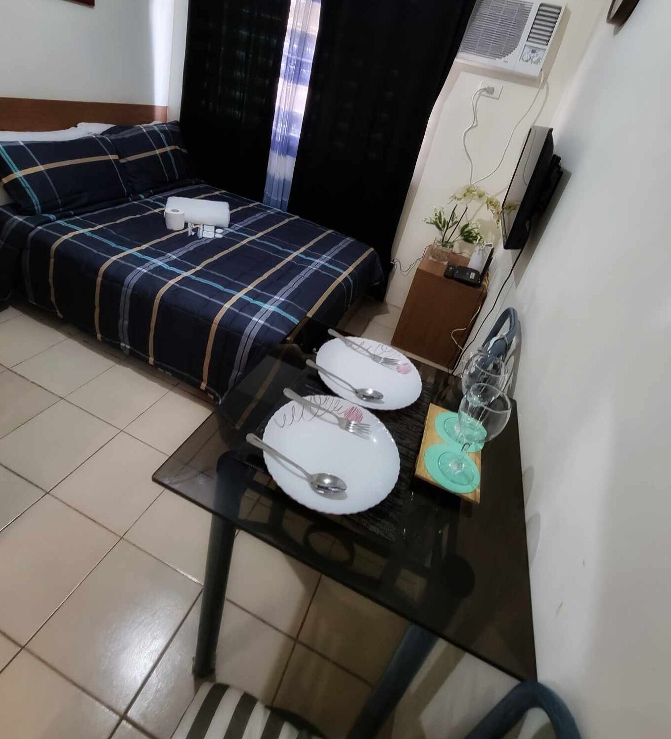 Une pièce comprenant un lit, une petite table avec des assiettes et des couverts, et une plante en pot.