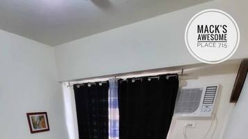 A small, tidy room with a bed, a small table with plates and cutlery, a TV, and a window with curtains.