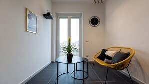 Een moderne woonkamer met een ronde zwarte tafel, een gele rieten stoel, een potplant en een groot raam met uitzicht.