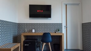 Een kamer met een flatscreen-tv waarop ‘NETFLIX’ staat, een bureau met een stoel, en behang met een patroon.