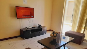 Ein modernes Wohnzimmer mit einem an der Wand montierten Flachbildfernseher, einem dunklen Holzschrank, einem Glastisch und einem braunen Sofa.