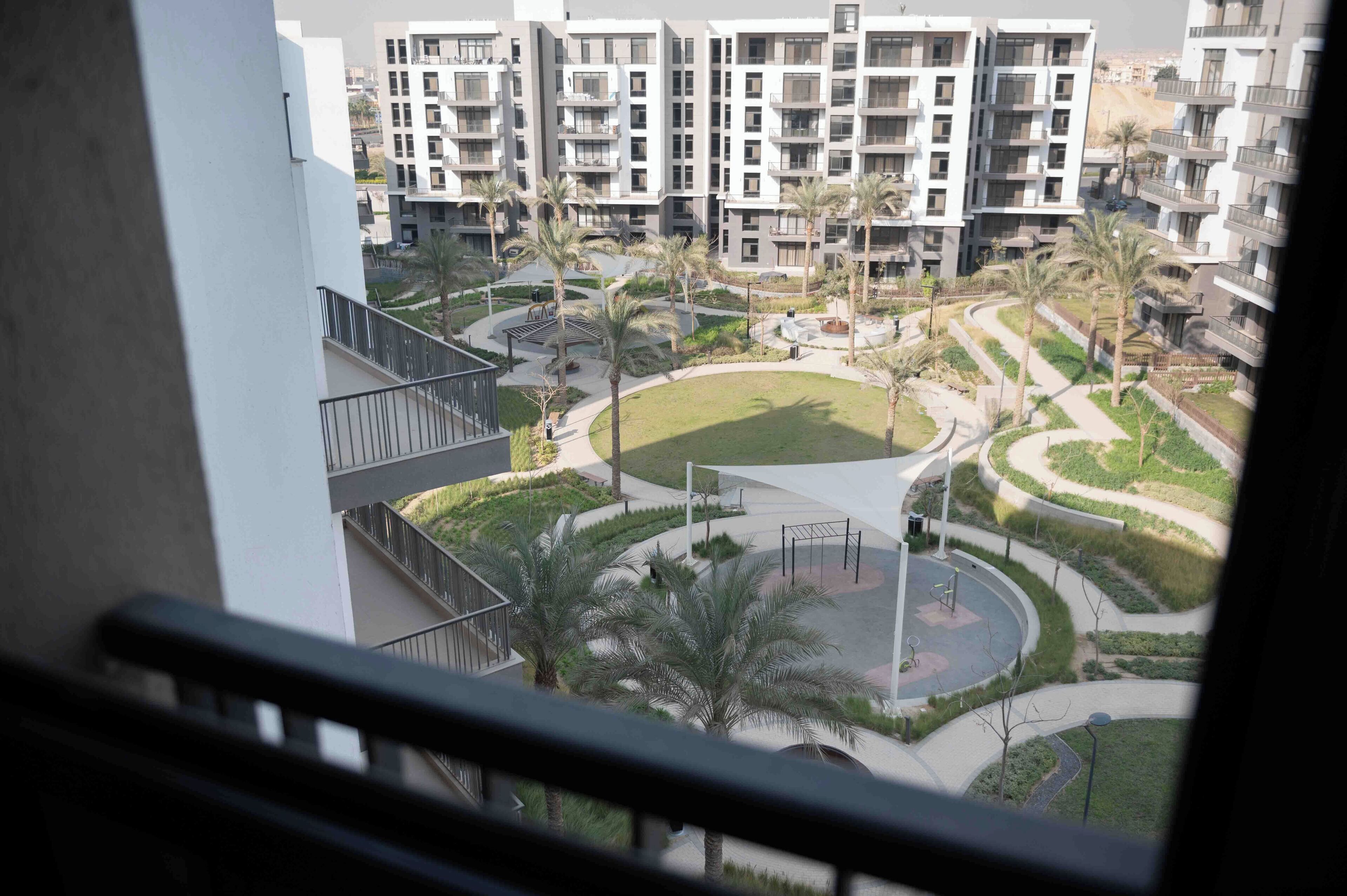 Complejo residencial con varios edificios de apartamentos, un área ajardinada central con palmeras y un paseo circular.
