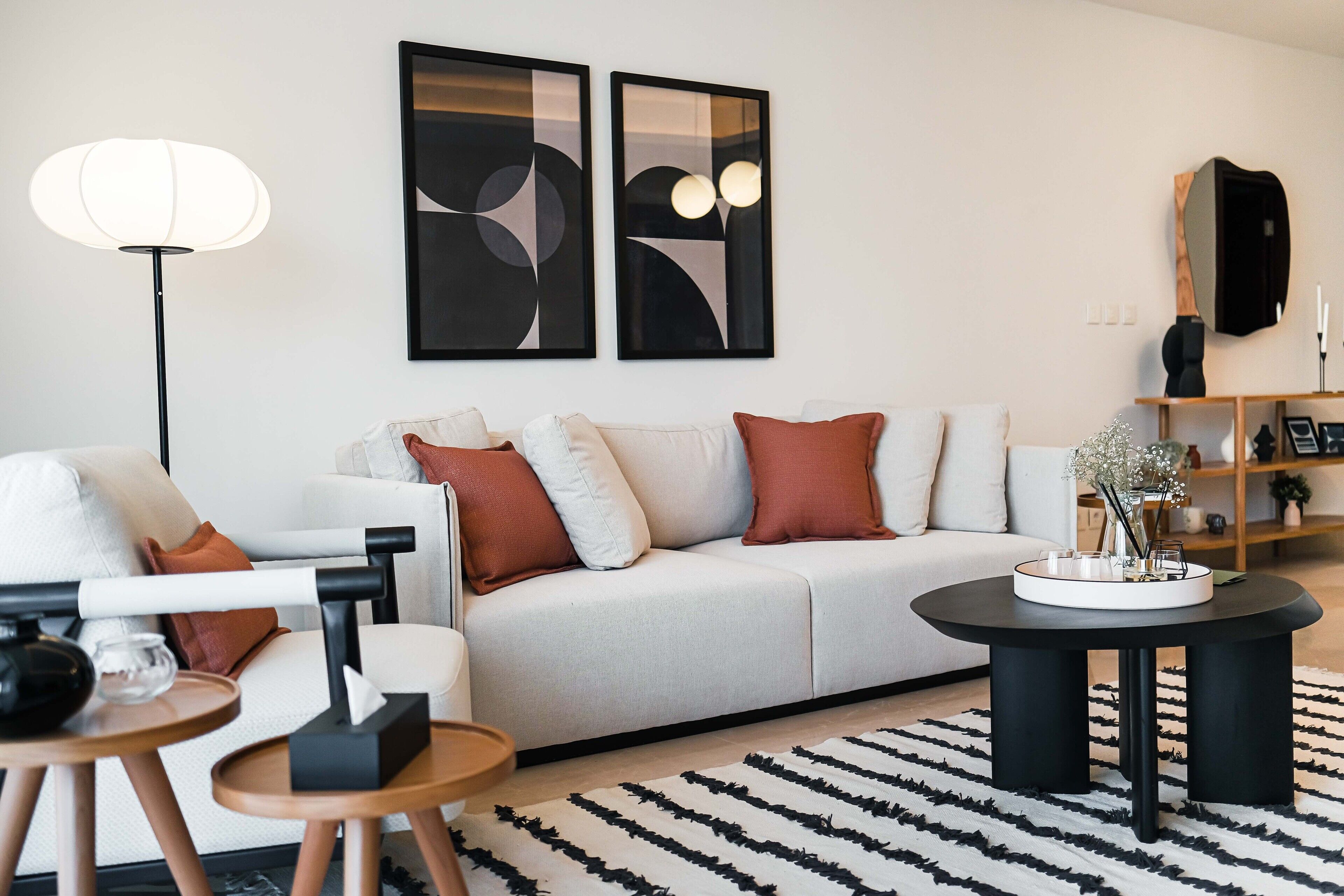 Een moderne woonkamer met een bank, salontafel en vloerlamp. Aan de muur hangen abstracte schilderijen en boven de bank is een spiegel.