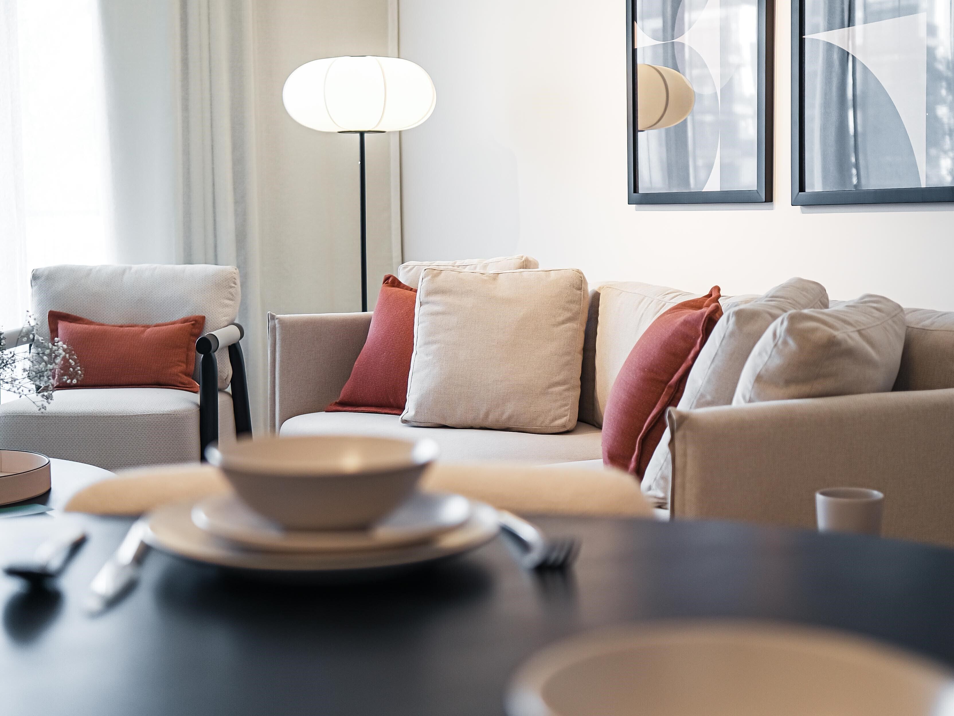 A modern living room with a sofa set, a dining table with a bowl and utensils, and a floor lamp.