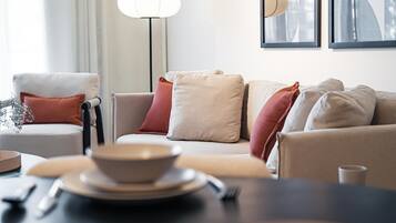 A modern living room with a sofa set, a dining table with a bowl and utensils, and a floor lamp.
