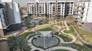 A modern residential complex with multiple apartment buildings, a central circular park with palm trees, and a fountain. - BIRD NEST at Cairo Festival City (New Cairo)