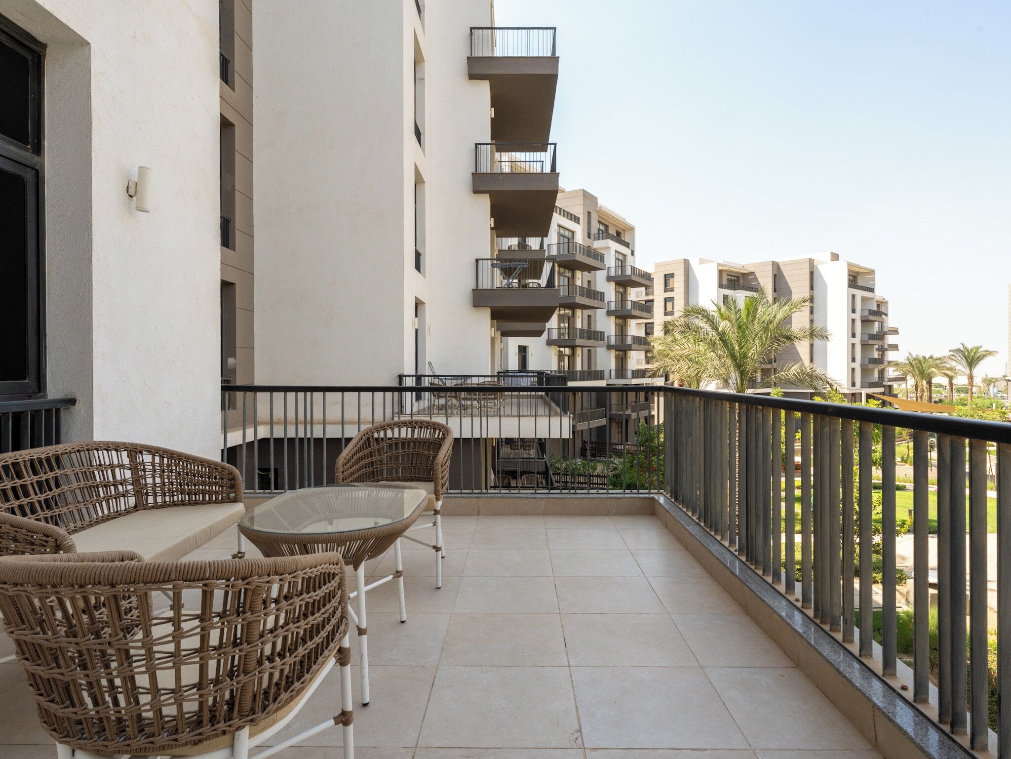 A balcony with wicker furniture, a tiled floor, and a view of adjacent buildings.