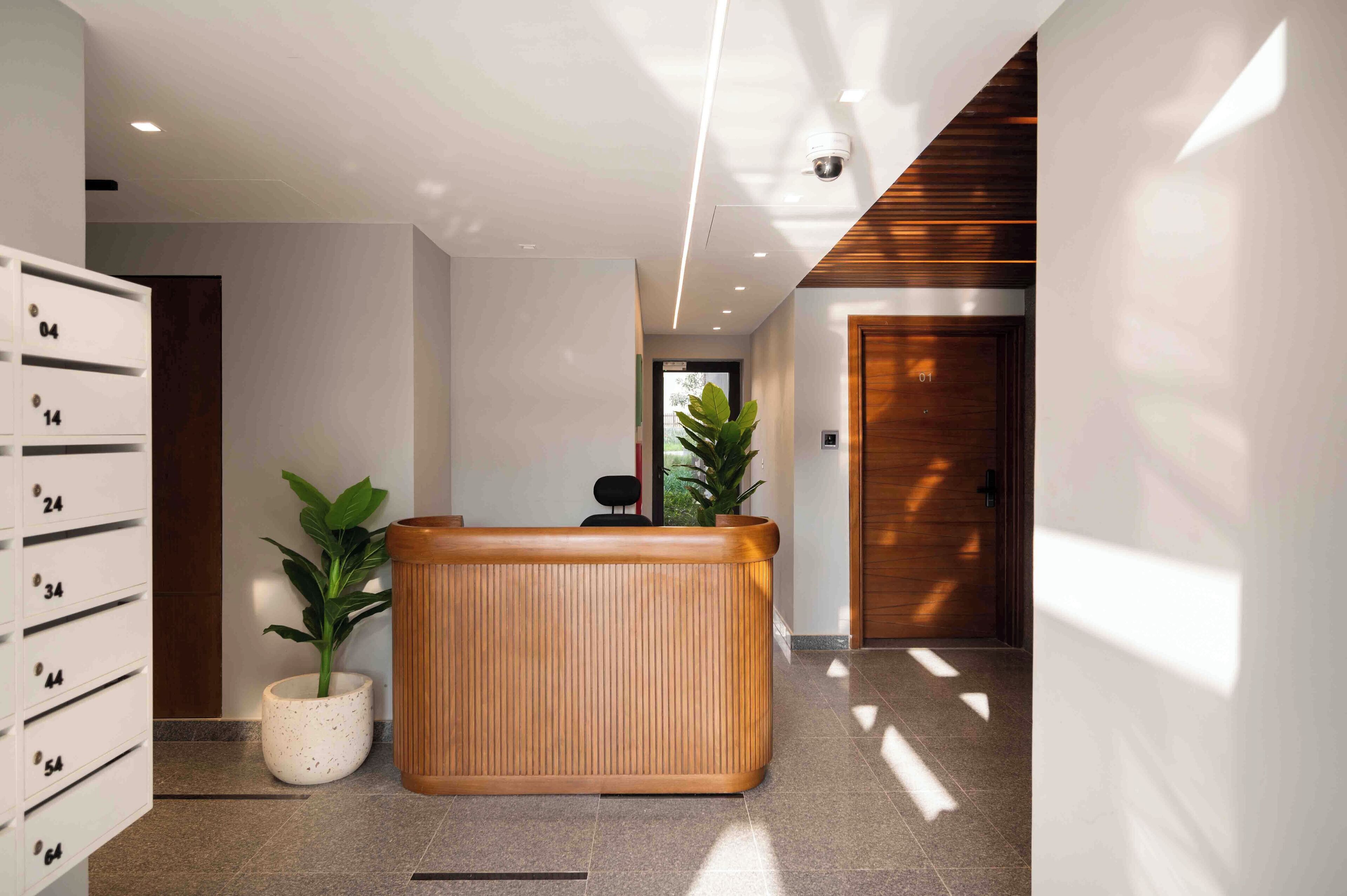 Un área de recepción moderna con un mostrador de madera, plantas en macetas y un sistema de números en la pared.