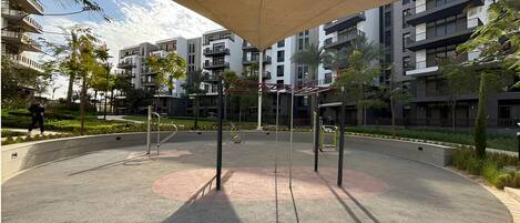 A circular outdoor area with a shaded seating area, surrounded by modern buildings and greenery.