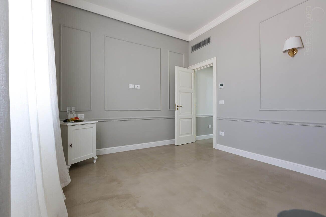 Ein Zimmer mit einer hellgrauen Wand, einer weißen Tür, einem kleinen weißen Schrank und einer weißen Stehlampe.