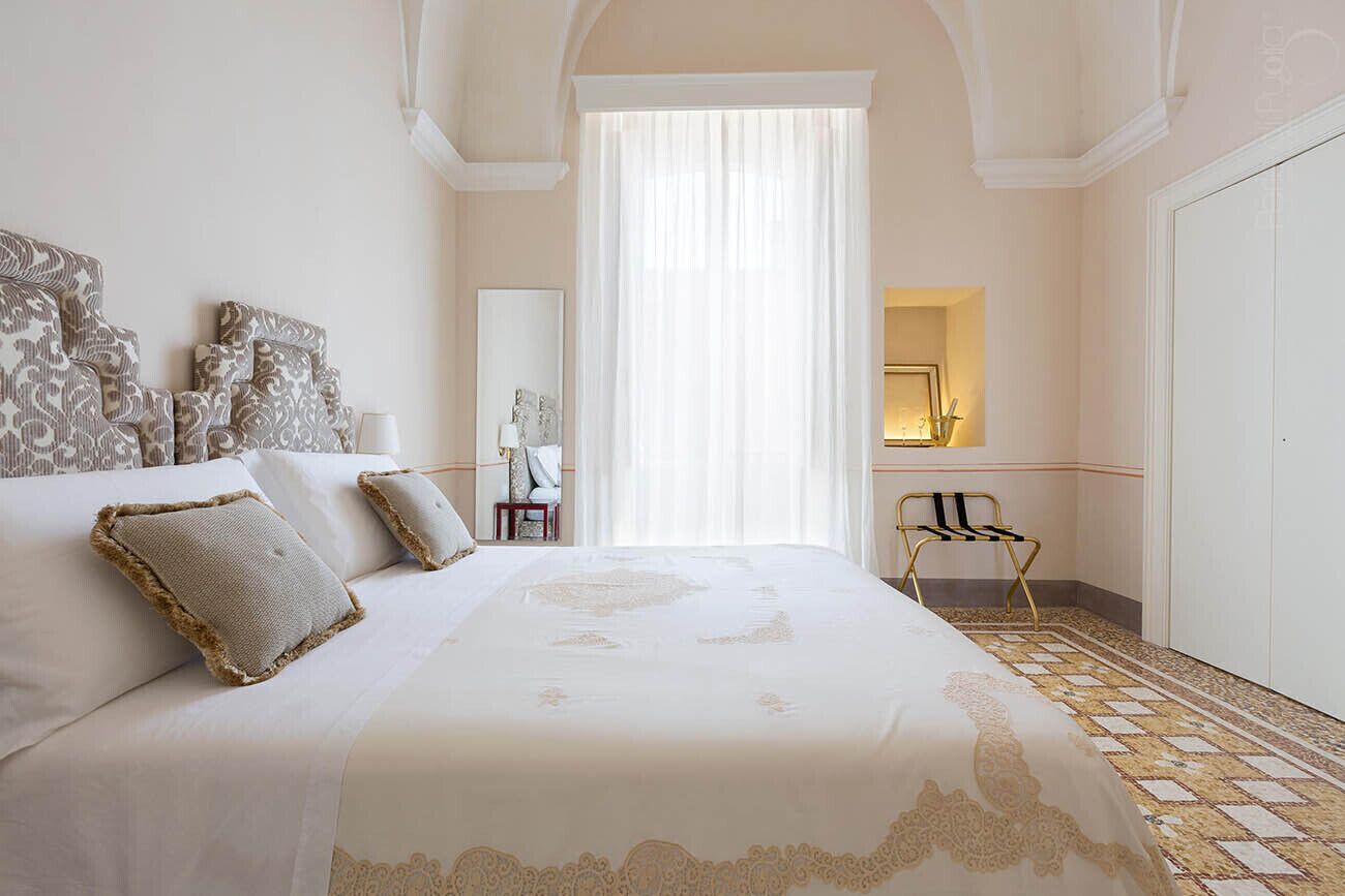 A spacious bedroom with a large bed, a sitting area with a chair, and a view of the outside through a window.