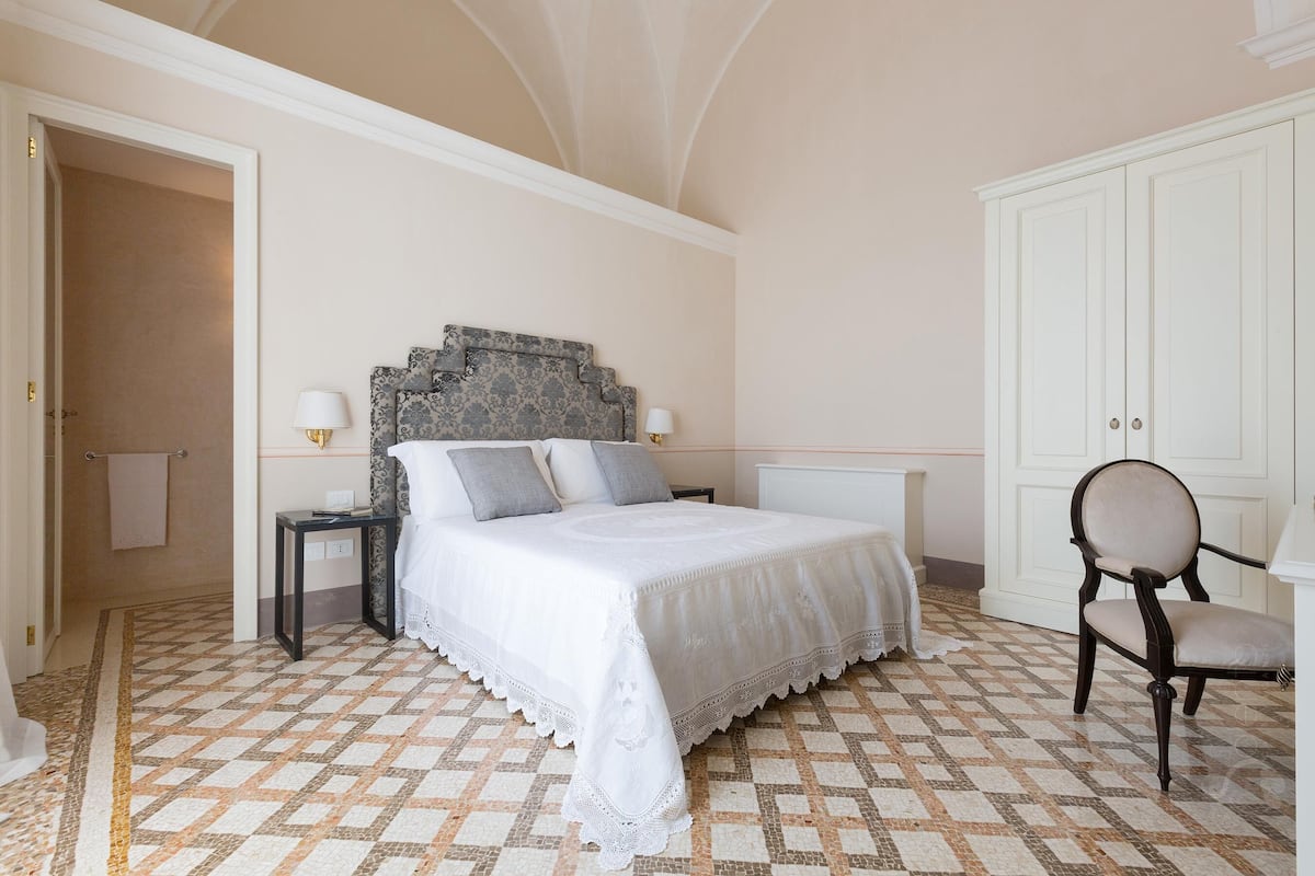 A bedroom with a large bed, a nightstand, a chair, and a wardrobe.