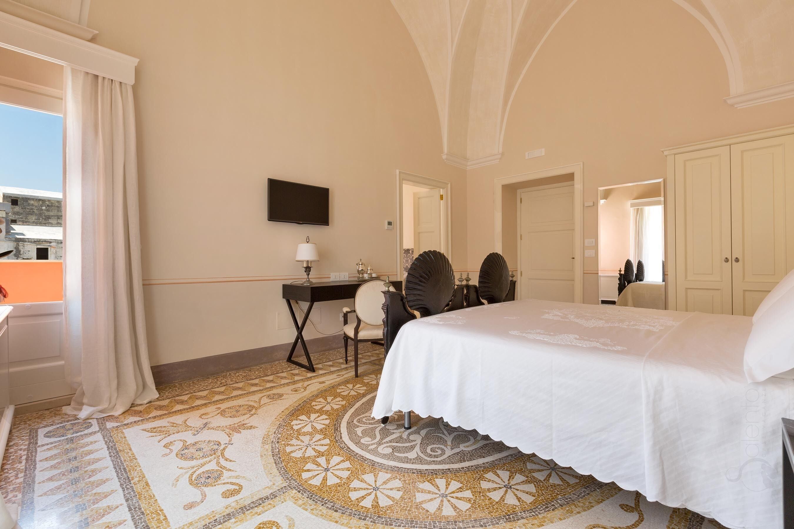 A hotel room with a bed, desk, chairs, and a television.