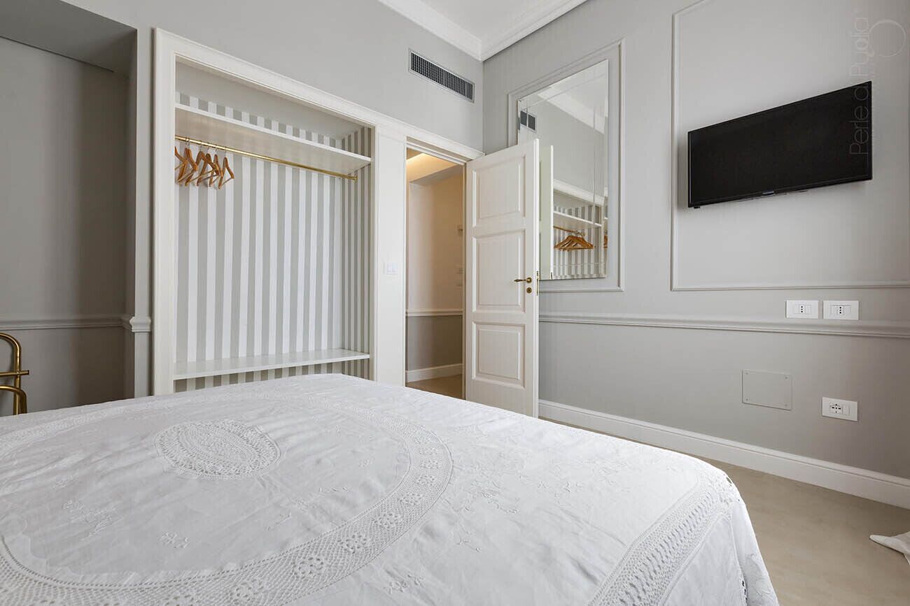 A bedroom with a large bed, a wardrobe, a mirror, and a television on the wall.