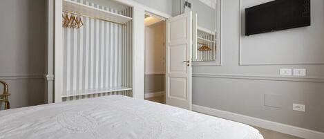 A bedroom with a large bed, a wardrobe, a mirror, and a television on the wall.