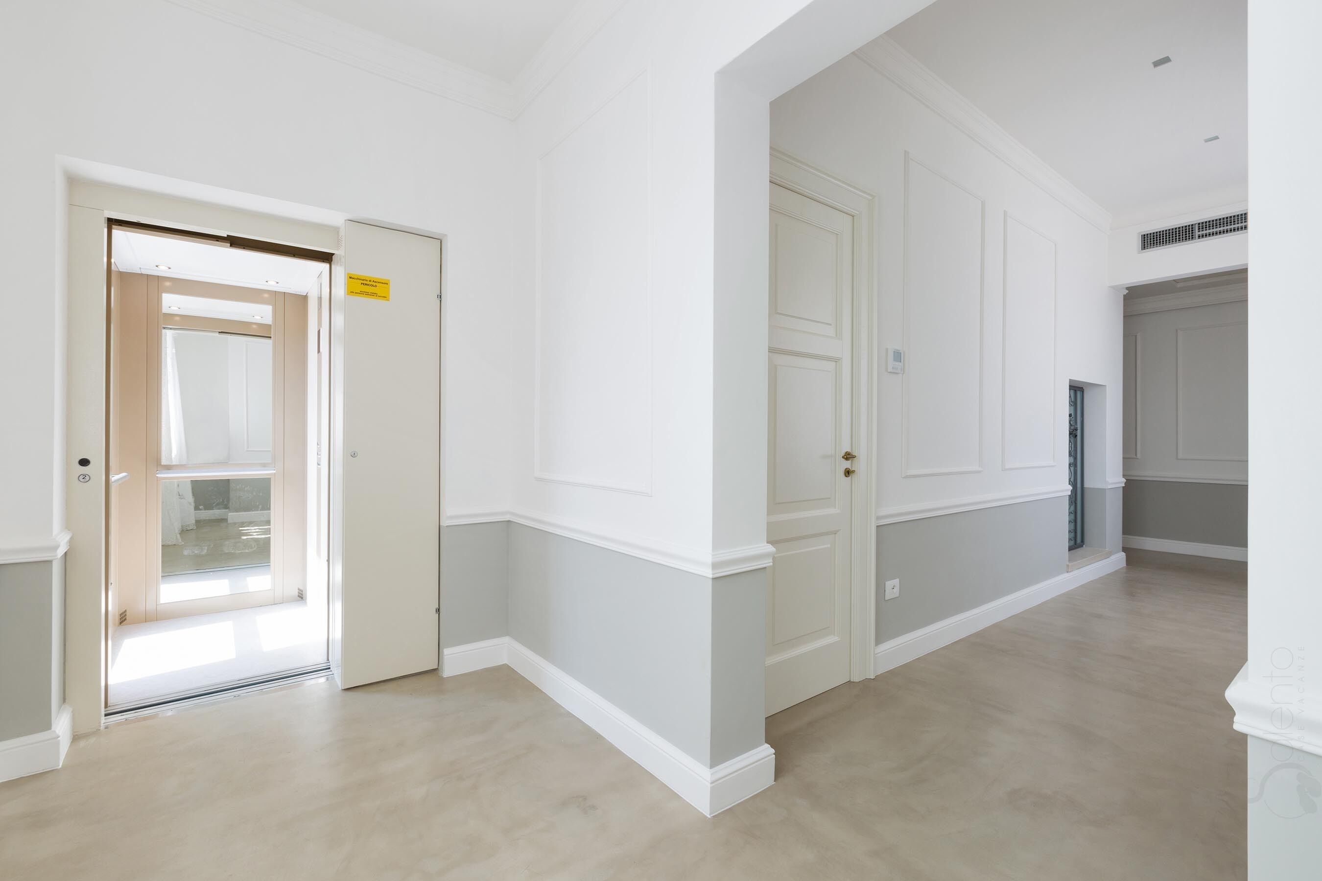 A spacious hallway with white walls and a light wooden floor, leading to a door with a sign.
