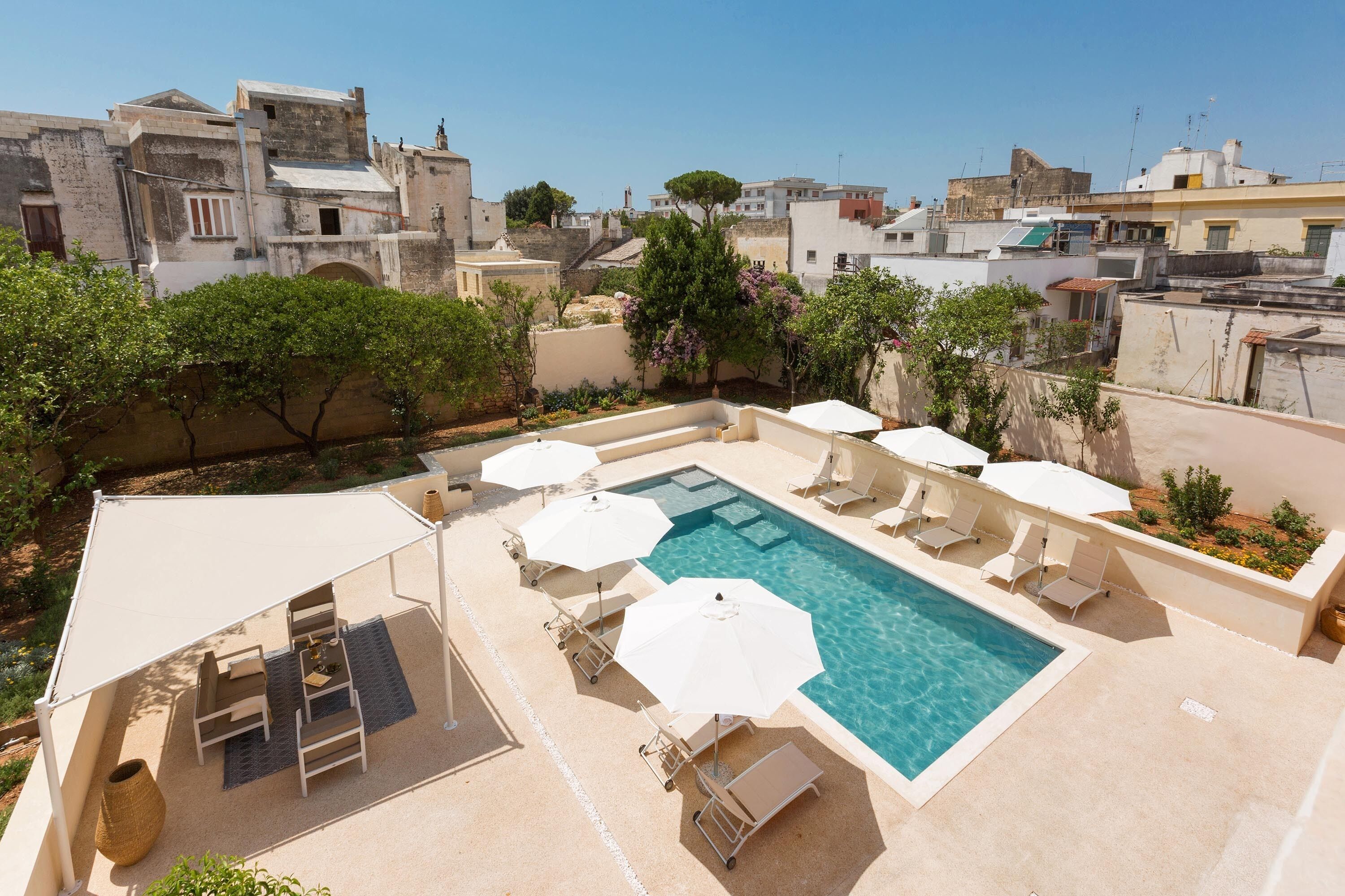Una piscina en la azotea con sillones y sombrillas, rodeada de árboles y edificios.