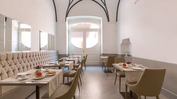 Un comedor con un banco largo, mesas y sillas, que destaca por un diseño moderno con techo alto y ventanas arqueadas.
