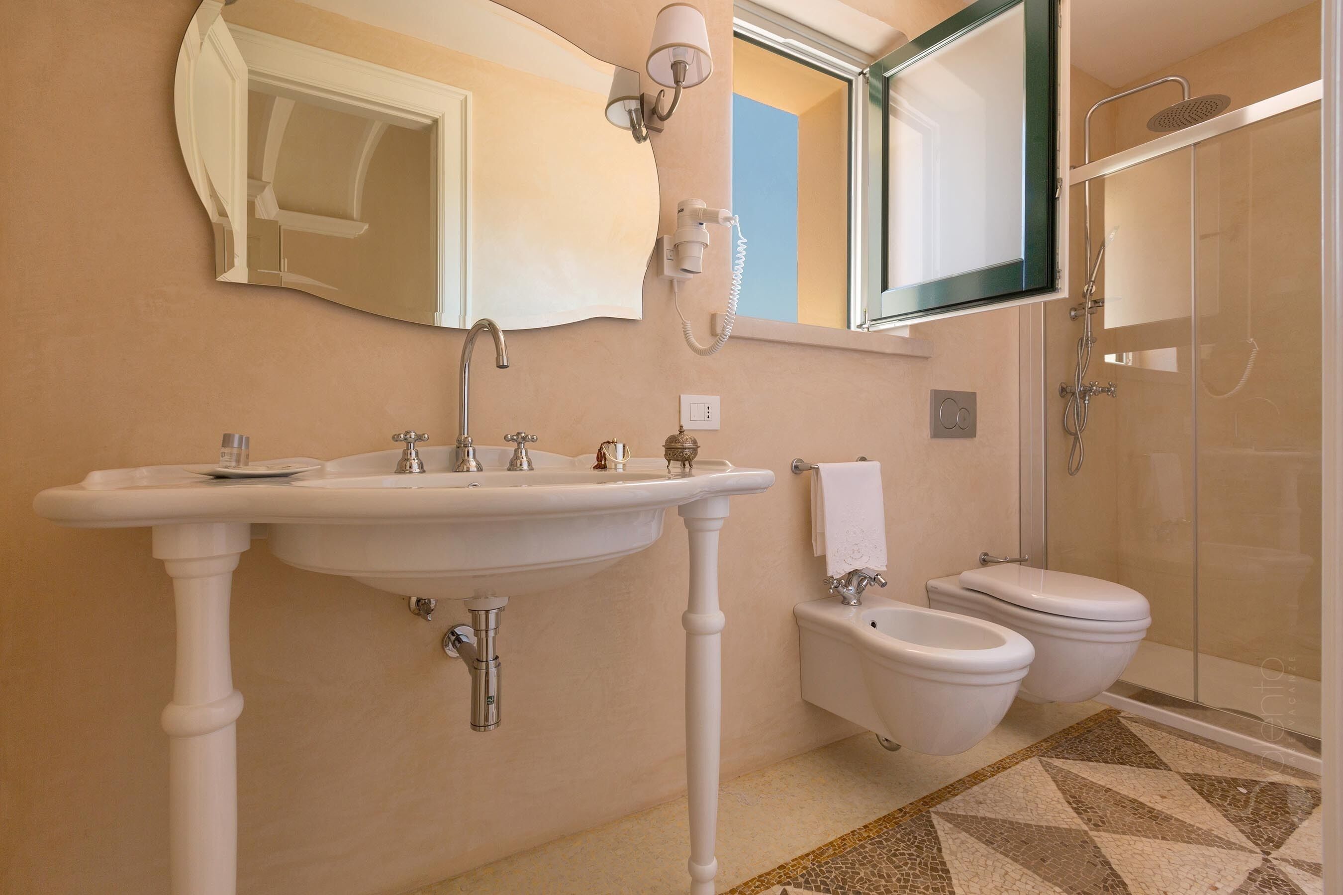 Un baño con lavamanos pedestal, un bidé, un inodoro, una ducha y un espejo.