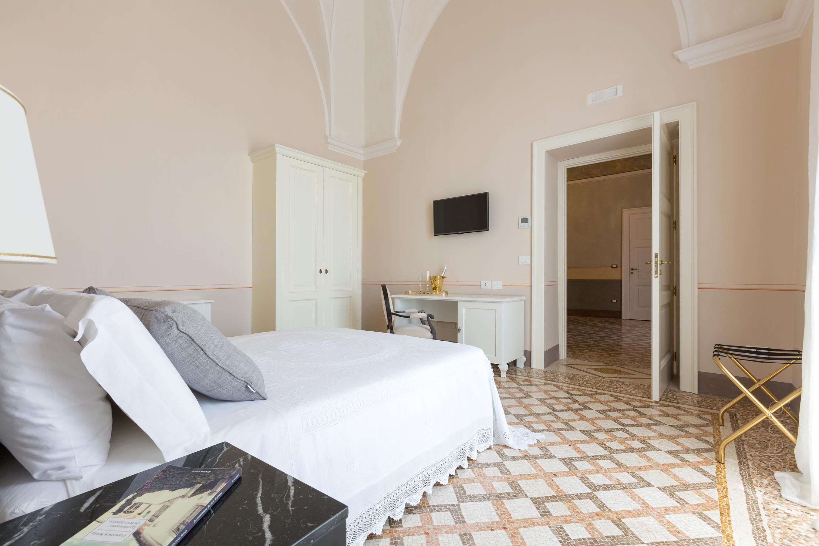 Habitación de hotel con cama, escritorio, televisión y baño visible a través de una puerta abierta.