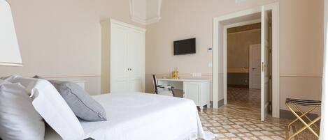 Habitación de hotel con cama, escritorio, televisión y baño visible a través de una puerta abierta.
