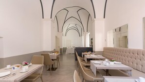 A spacious dining area with high arched ceilings, multiple tables and benches, and a neutral color palette. - Palazzo Fasti (Casarano)