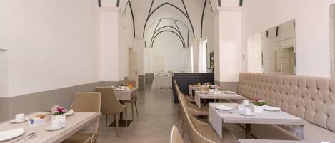 A spacious dining area with high arched ceilings, multiple tables and benches, and a neutral color palette.