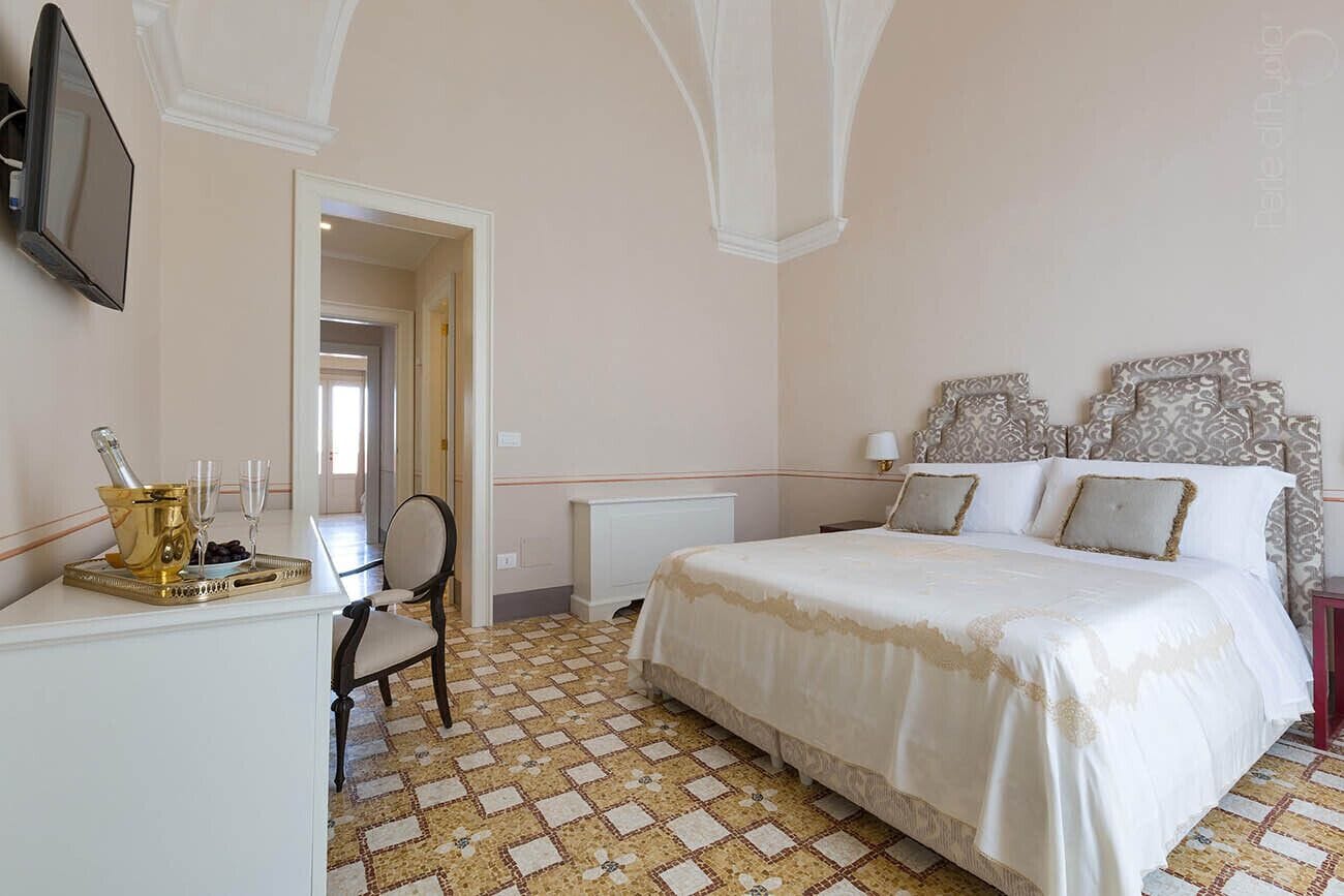 A bedroom with a bed, a desk with a tray of champagne, a chair, and a television on the wall.