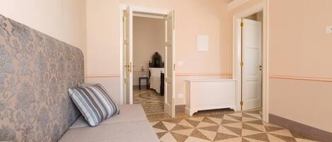 Quarto de hotel com cabeceira estampada, um sofá, tapete estampado e chão com padrão geométrico.
