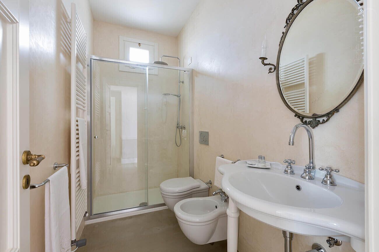 A bathroom with a glass-enclosed shower, a toilet, a bidet, and a sink with a mirror.