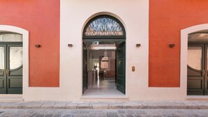 A building entrance with a central archway, flanked by two green doors, and a clear pathway leading inside. - Palazzo Fasti (Casarano)